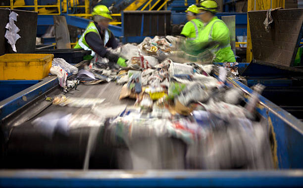 Workers separating paper and plastic on a conveyor belt in a recycling facility